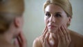 Upset woman looking in mirror and touching face, sad about skin aging, wrinkles