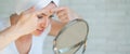 An upset woman looks in the mirror and squeezes a pimple on her forehead. A girl with hormonal problems cleanses her Royalty Free Stock Photo