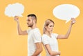 Upset woman and man holding paper thought bubbles over yellow background