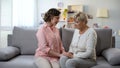 Upset women sitting on sofa and holding hands, health problems, support and care