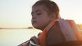 Upset and worrying young girl kid looks into the water sitting in the kayak along tranquil sunset lake