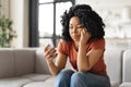 Upset Young African American Woman Sitting On Couch And Looking At Smartphone Royalty Free Stock Photo