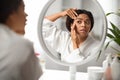 Upset young black woman checking wrinkles around eyes near mirror at home Royalty Free Stock Photo