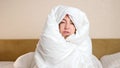 Upset frozen woman with duvet sits on bed in cold room