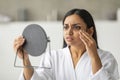 Upset young indian woman looking at mirror, touching her cheeks Royalty Free Stock Photo