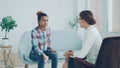 Upset young lady in casual clothing is having therapy session with psychologist in light studio. Girl is talking and Royalty Free Stock Photo