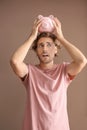 Upset young man with piggy bank on color background