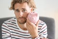 Upset young man with piggy bank at home