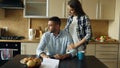 Upset young man reading unpaid bills and hugged by his wife supporting him in the kitchen at home Royalty Free Stock Photo