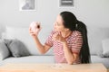 Upset young woman with empty piggy bank at home