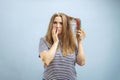 Upset young woman looking with shock at her damaged hair on blue background Royalty Free Stock Photo