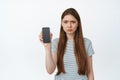 Upset young woman showing her phone screen and frowning disappointed. Girl holds smartphone, shows mobile screen with Royalty Free Stock Photo