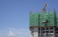 Upward view of precast building cover by green net, large tall Tower Crane moving machine in construction work, under clear blue