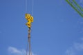 The upward view of yellow steel loop and chain hanging on the sling of a large green beam tower crane arm`s under clear blue sky