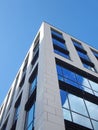 Upwards view of the corner of a white modern office building with blue sky and clouds reflected in large glass windows Royalty Free Stock Photo