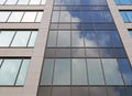 upwards view of the facade of a modern office buildings with blue sky and white clouds reflected in the rows of geometric windows Royalty Free Stock Photo