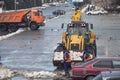 Road maintenance workers in orange vests throw snow into a tractor bucket.