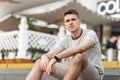 Urban attractive young man in a fashionable T-shirt in beige stylish shorts is resting sitting on the steps in the city. Royalty Free Stock Photo