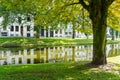 Urban building reflected in calm water of canal running through city under large leafy tree Royalty Free Stock Photo