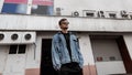 Urban cool young hipster man in youth stylish clothes in trendy sunglasses stands near a vintage white building in the city on a