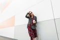Urban cool young woman with red lipstick in casual youth outfit in sunglasses stands with cup of hot drink near modern building in