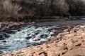 Urban creek with water flowing over and around large rocks, winter landscape