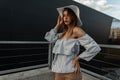 Urban elegant young woman fashion model in fashionable straw white hat in vintage shirt rests in city near modern black building. Royalty Free Stock Photo