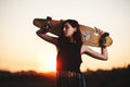 Urban fashionable girl with longboard posing outdoors on the road at sunset.