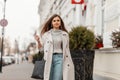Urban fashionable young woman walks outdoors in the city. Modern brown-haired girl model in stylish outerwear with a trendy Royalty Free Stock Photo
