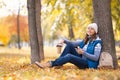 Urban golden autumn. Attractive smiling woman in warm wear sits under a tree with coffee and mobile and chill out in the