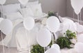 Urban jungle and bunch of white balloons in trendy bedroom with king size bed with white bedding and grey blanket