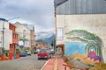 Urban landscape of cars on the streets of Ushuaia, Argentina, with snowy mountains between colorful buildings, against a