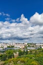 An urban landscape with a green park, residential areas and a TV tower against a bright blue sky with thickening clouds