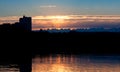 Urban landscape. Sunset in city. Silhouettes of houses against background of setting sun and setting sky are reflected in dark Royalty Free Stock Photo