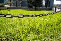 Urban lawn with fresh green grass fenced forged chain, the background trees and buildings, spring day.