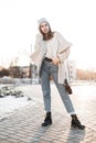 Urban model of a beautiful young woman in stylish youth warm seasonal outerwear and boots on a background a bright amazing sunset