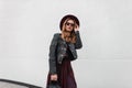 Urban modern young woman hipster in fashionable clothes with a leather backpack in a purple hat posing standing Royalty Free Stock Photo