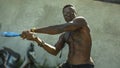 Urban portrait of young aggressive and upset violent black afro American man using baseball bat threatening at grunge corner in