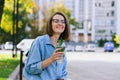 Urban portrait of young business woman in eye glasses, t- shirt, trousers is walking in the city street. Drinking healthy drink Royalty Free Stock Photo