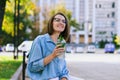 Urban portrait of young business woman in eye glasses, t- shirt, trousers is walking in the city street. Drinking healthy drink Royalty Free Stock Photo