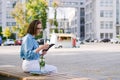 Urban portrait of young business woman in eye glasses, t- shirt, trousers is walking in the city street. Drinking healthy drink Royalty Free Stock Photo