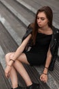 Urban pretty fashionable young woman in in stylish autumn black clothes in leather vintage boots is resting sitting on stone steps Royalty Free Stock Photo