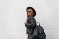 Urban pretty young hipster woman in trendy dark sunglasses in a chic hat in a leather jacket with a black stylish backpack Royalty Free Stock Photo