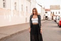 Urban pretty young woman in a long vintage black skirt in an elegant white top in a fashionable leather jacket stands on the road Royalty Free Stock Photo