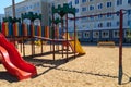 Urban residential infrastructure without people - children`s playground next to a condominium. Swing, slide, stairs, multistory