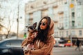 Urban shot of a fashionable woman in sunglasses and stylish hoodie hugging her small dog - york terrier, busy city street on a Royalty Free Stock Photo