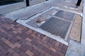 Urban sidewalk of mixed brick, stone, cracked and patched concrete, and metal grates