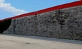 Urban street background. Asphalt road alongside a wall made of little concrete blocks with red edge on top