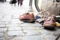 Urban street composition. Pair of brown leather boots with white shoelaces, light beige pullover on cobblestone pavement