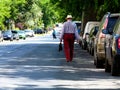 Urban street in diminishing perspective with parked cars and elderly man walking away in white hat